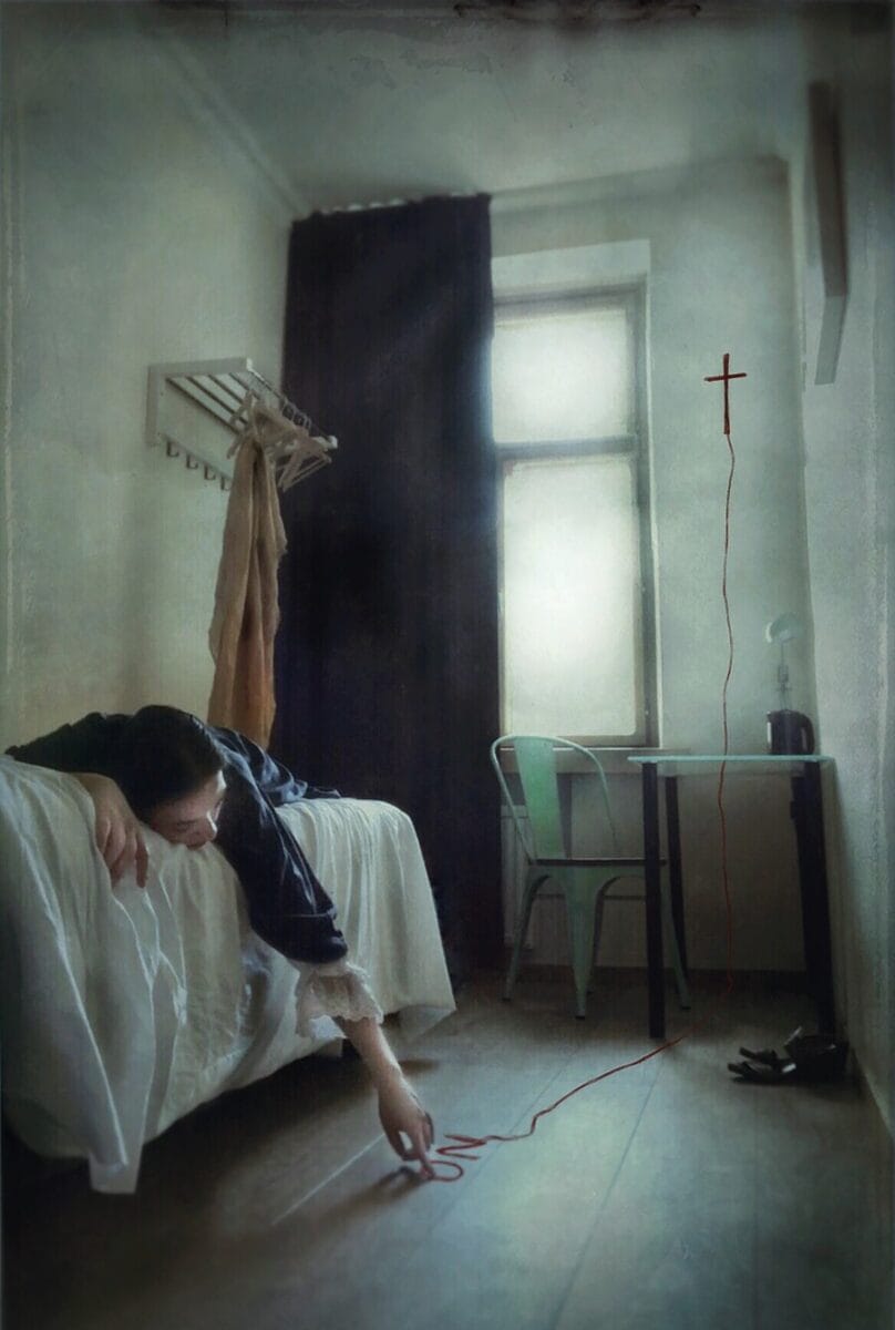 Ana Priscila Rodriguez photograph of woman lying on a bed with her hand drawing words on the floor