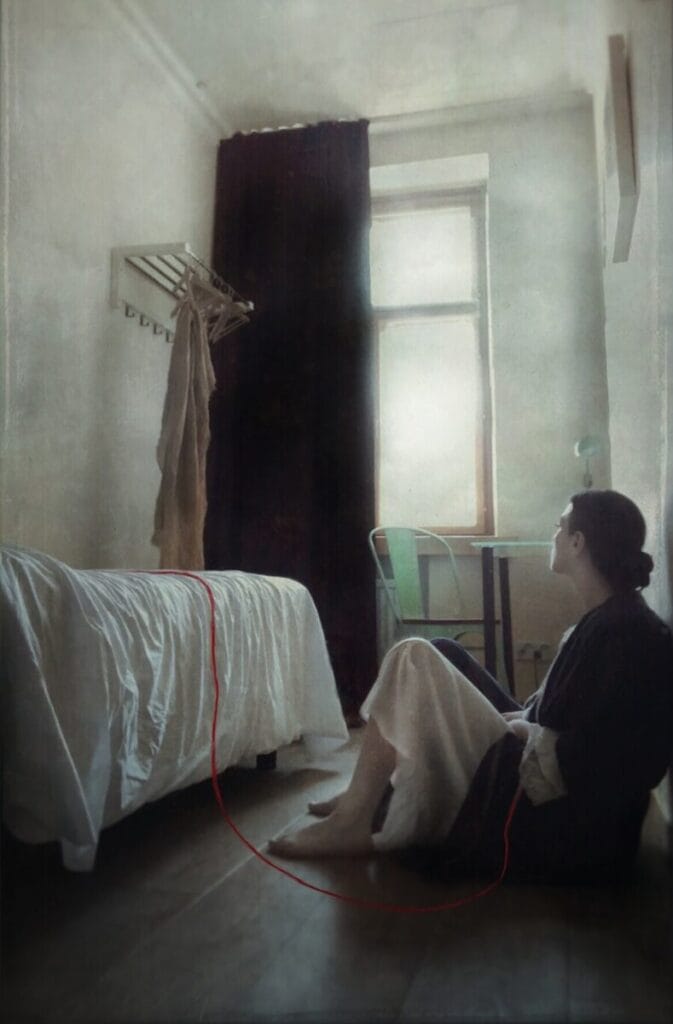 Ana Priscila Rodriguez photographs of woman sitting on the floor in a small bedroom with a red line attached to her body